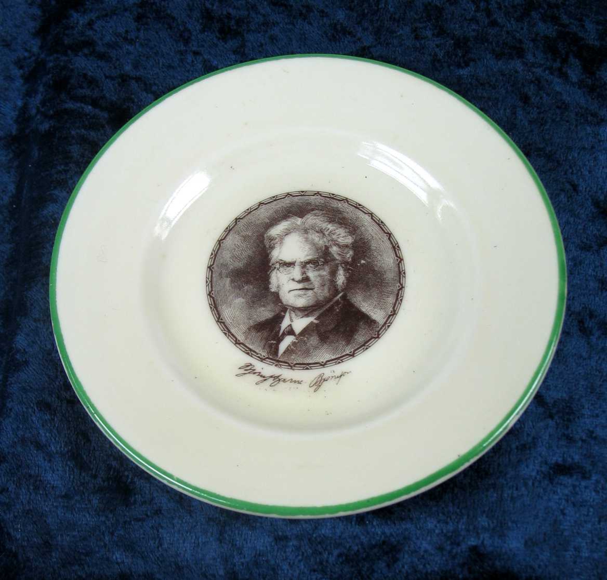Hvit skål i porselen med grønn kant ytterst og trykt portrett i midten.