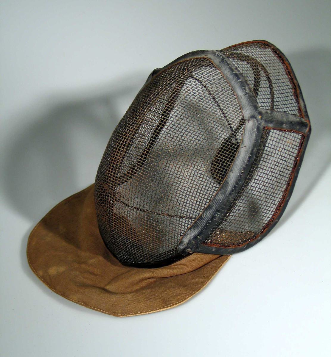 Fektemaske laget av metallgitter med bøyle bak og tettvevet dobbelt stoff foran for å beskytte halsen.