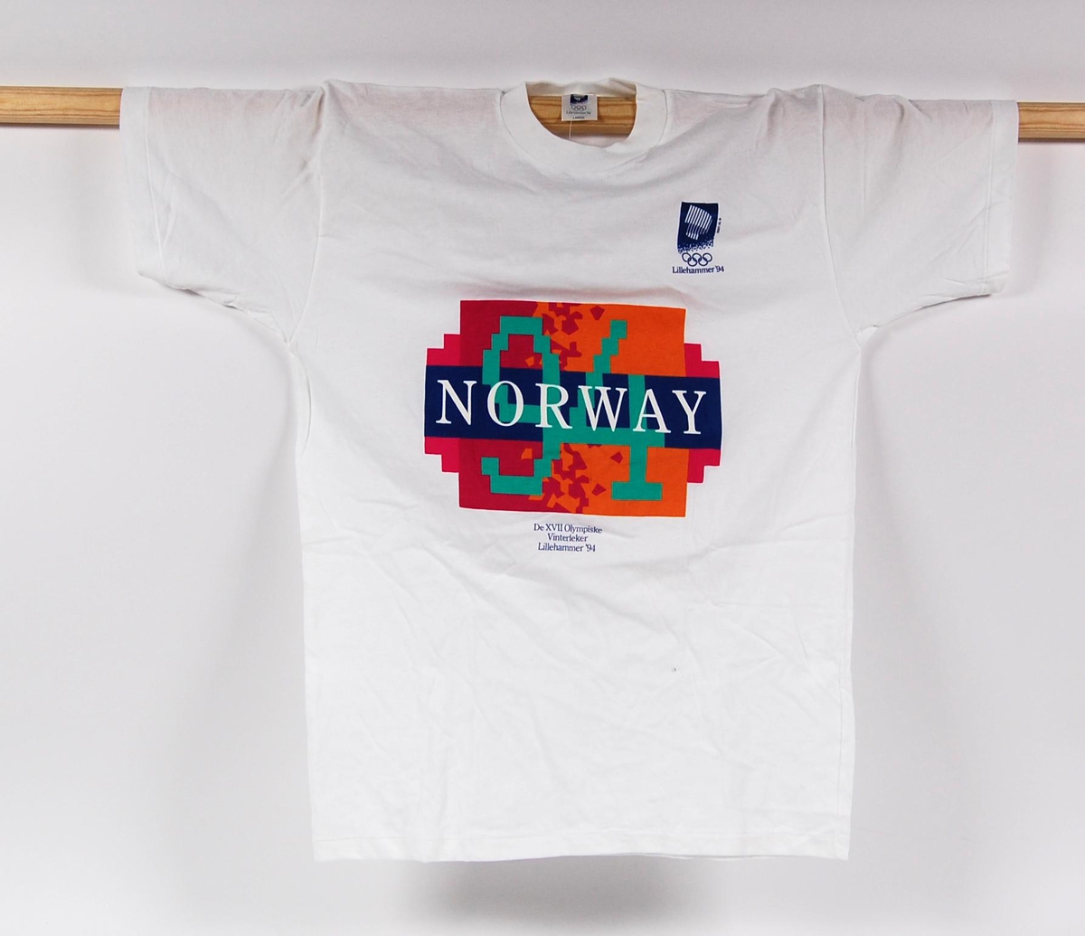 Hvit t-skjorte med 2 logoer for de olympiske vinterleker på Lillehammer i 1994. Den ene logoen er flerfarget og har krystallmønster. Krystallmønsteret inngikk i LOOCs designprogram. T-skjorten er i størrelse L.