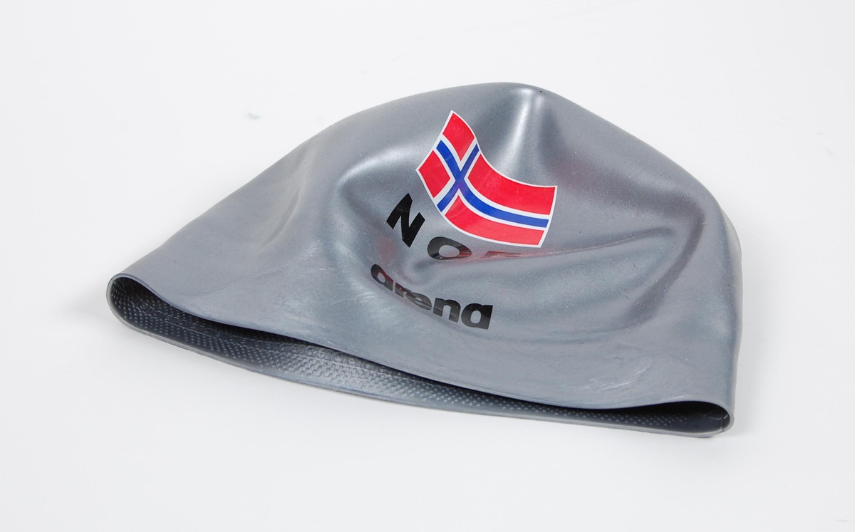 Sølvfarget badehette av latex med to laminerte norske flagg. 