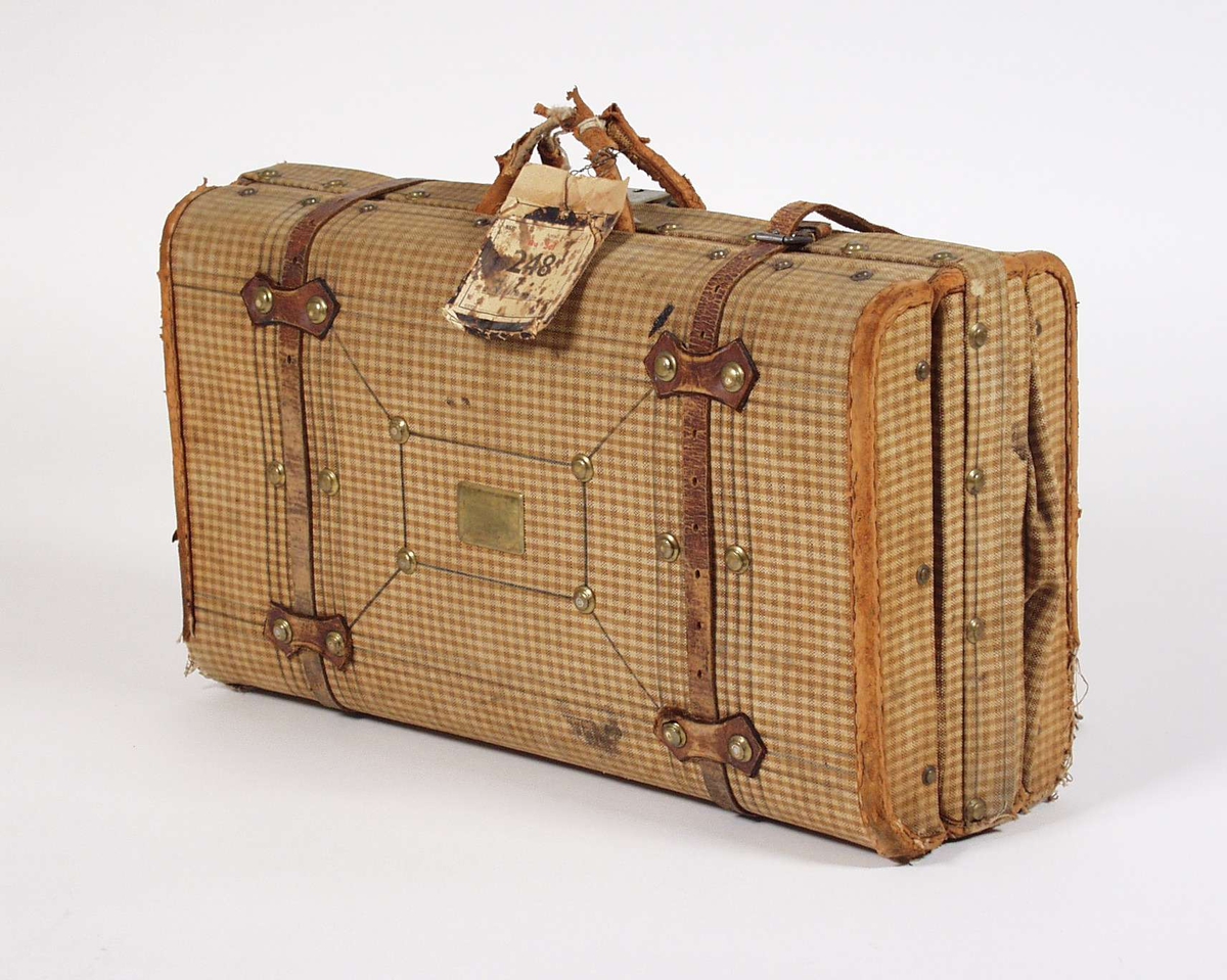 Kofferten er laget av tre og papp. Utvendig er den trukket i brun-og-hvit-rutet tekstil og har lås av messing. På ene siden er det også festet en messingplate. Kantene er forterket med skinn og to lærbelter holder kofferten skikkelig sammen.En godslapp er festet til håndtaket som også er i skinn. Innvendig er den kledd med blå-og-hvit-stripet tekstil. Kofferten er delt i to rom med en plate imellom, på denne er det festet en lomme av brunt skinn. Tekstilremmer skal holde innholdet på plass. Kofferten innholder en del ulike papirer blant annet et Aftenposten fra 1913 og et fra 1917.