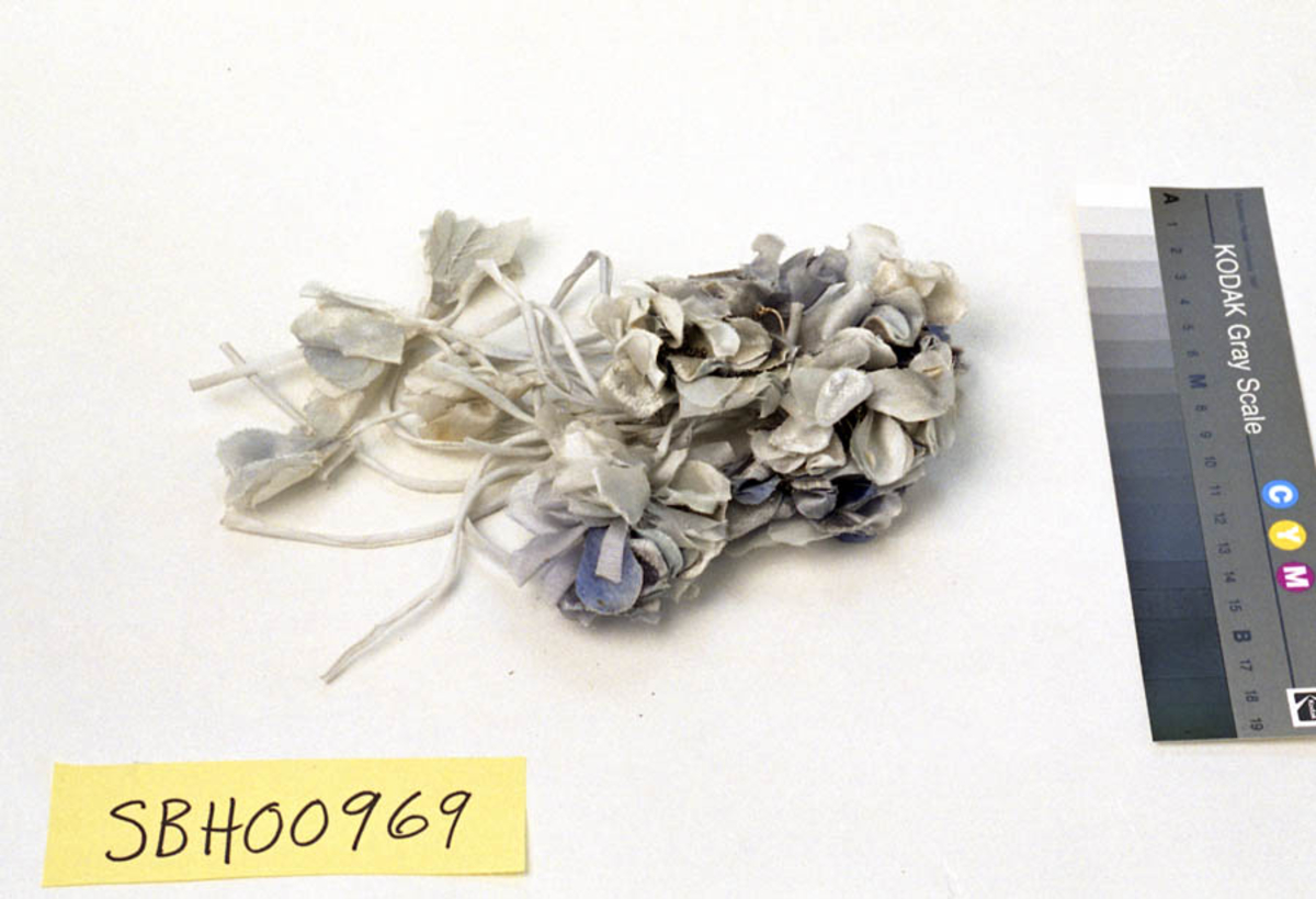 Form: Bukett av stoffblomster som er surret sammen med tape på midten, med blomstene i ene enden. 
