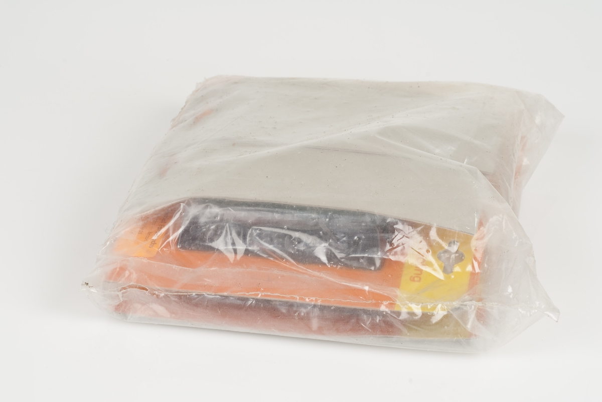 Fargevoks i papp- og plastpakning.
To fargevoks (en sort og en brun) i en pakning.
Pakningen er gul og orange med en orange påklistret merkelapp.
Pakningene ligger samlet i en plastpakning.