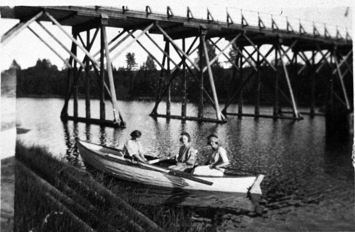 Kjelleholen Bru. Trebru, som ble revet omkring 1939 i forbindelse med veiutbygging. Under brua sitter tre unge damer i en robåt med ror. 