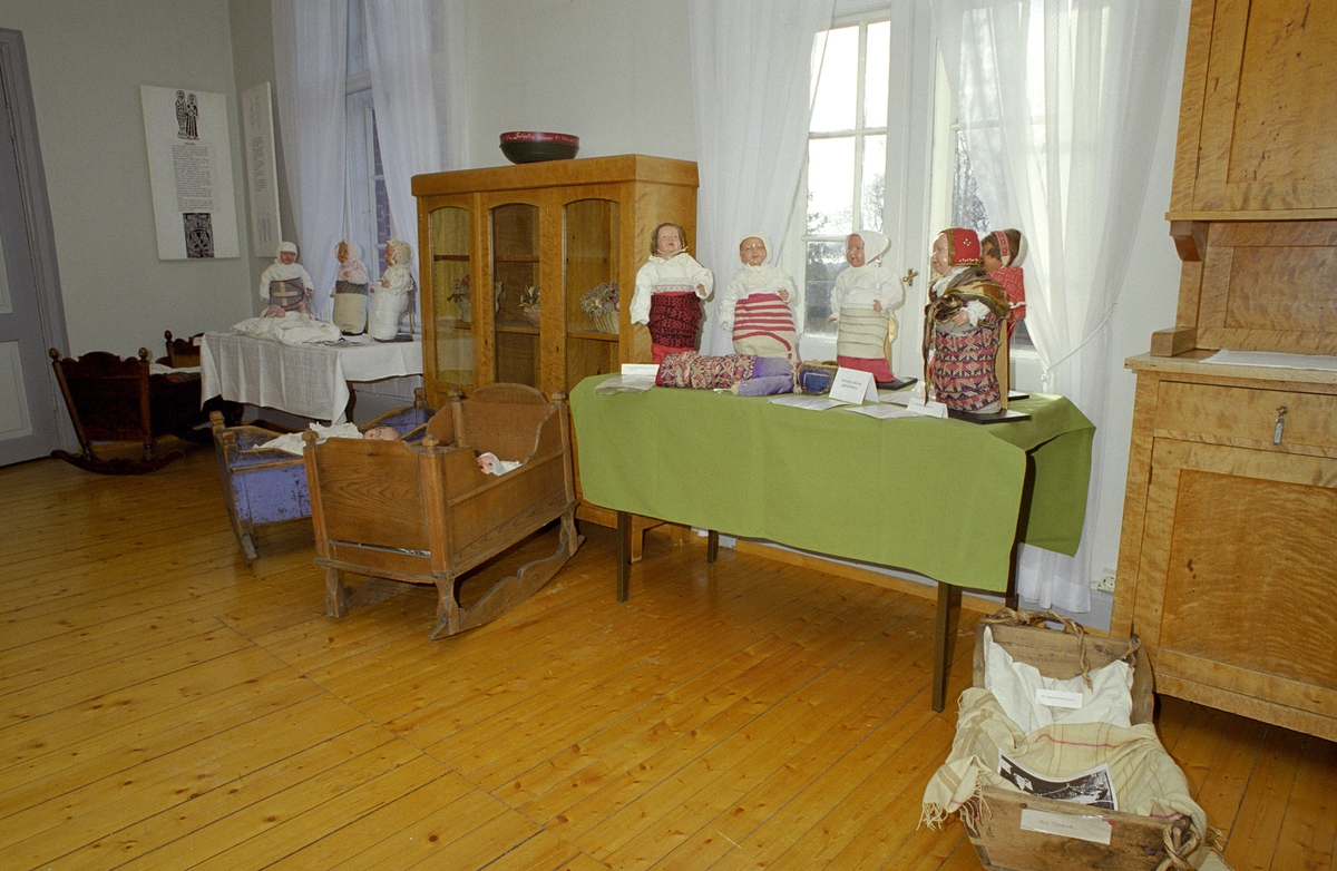 Utstilling. Katti Anker Møller. Bord med dukker, kumser, klær og vugger.