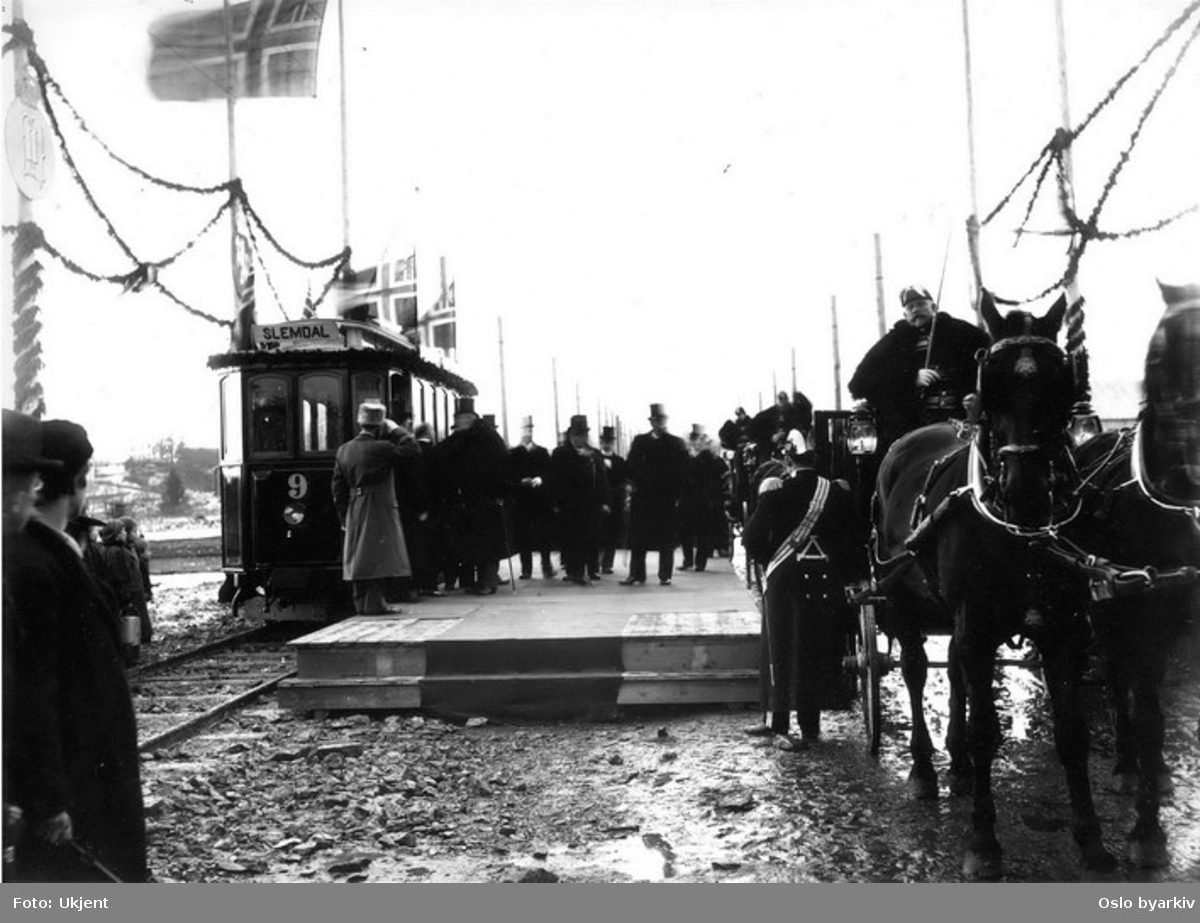 Kong Oscar 2. på Norges besøk i mars 1898, kong Oscar går på "kongeplattform", kongens vogn med hester, Holmenkollbanens vogn 9. Norske flagg med unionsmerket, koffardiflagg.