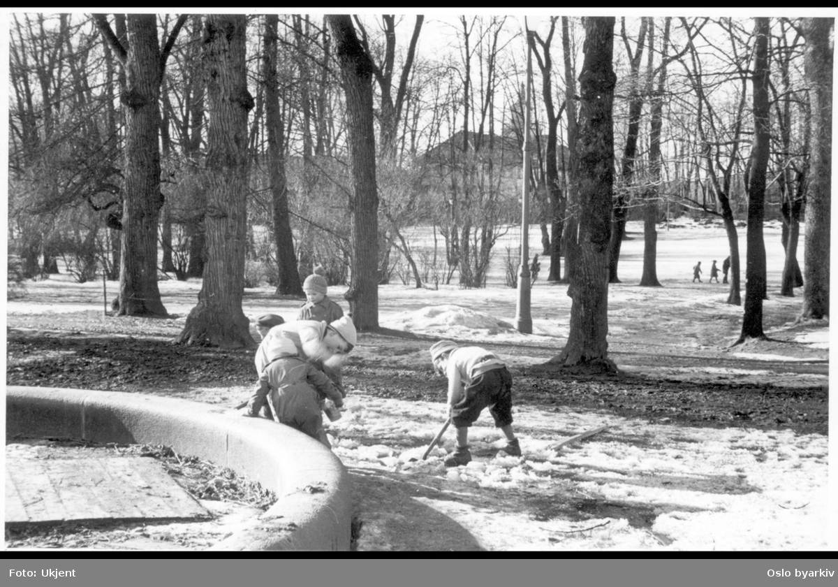 Vinter i Frognerparken. Lekende barn med spade på skarasnø ved lekeplassen sørøst i parken. Bildet tatt vestover mot Frogner Hovedgård (Bymuseet) i bakgrunnen. Vintertappet plaskedam.
