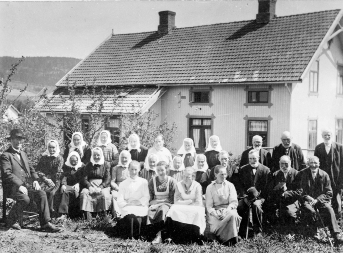 24 personer utenfor Veldre gamlehjem (Fagertun under Koss), Byflaten, Ringsaker. Pastor Reinert Svendsen sitter til venstre.