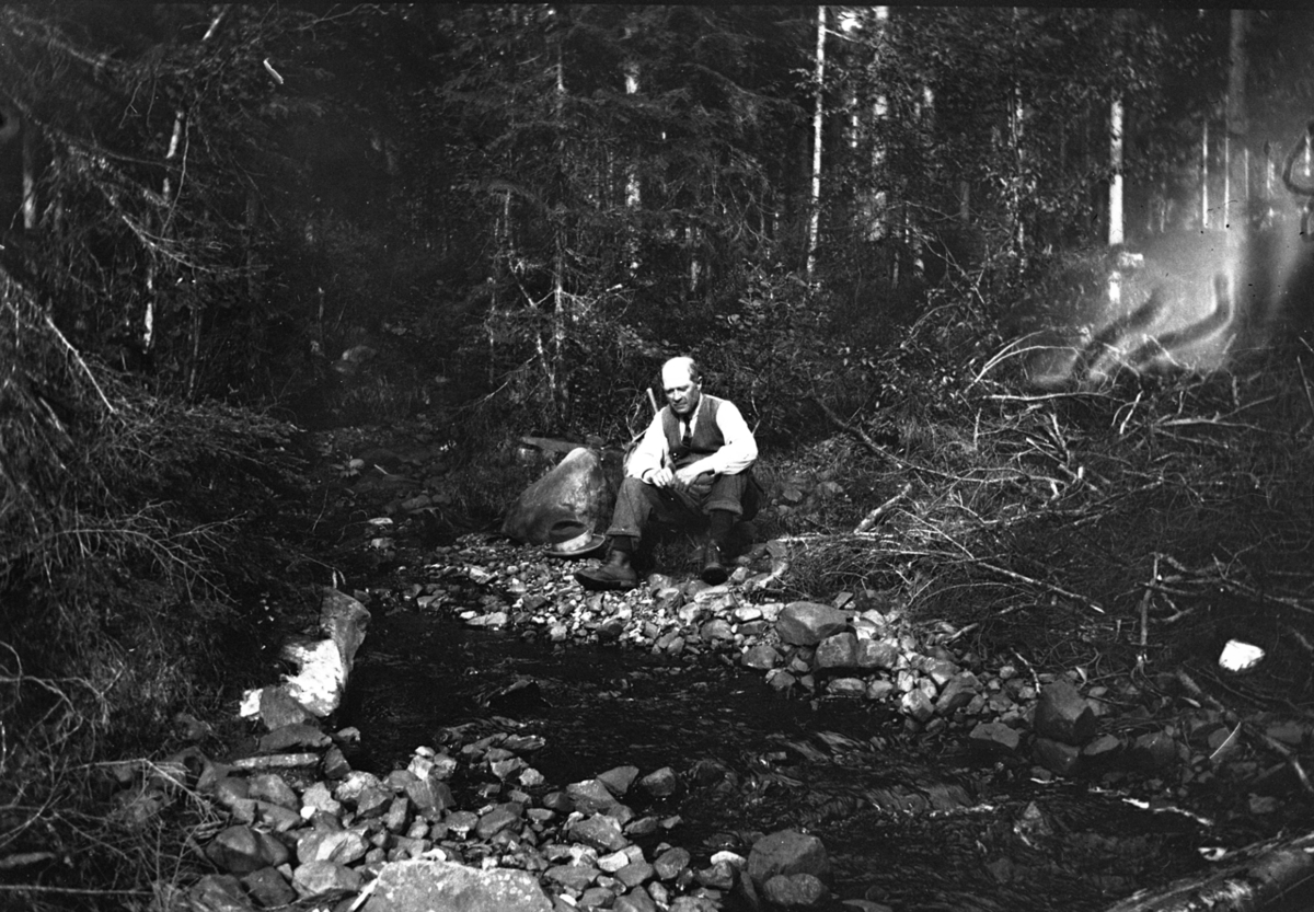 En mann sitter i skogen. 
Sigvart Jørgensen (1871-1940).