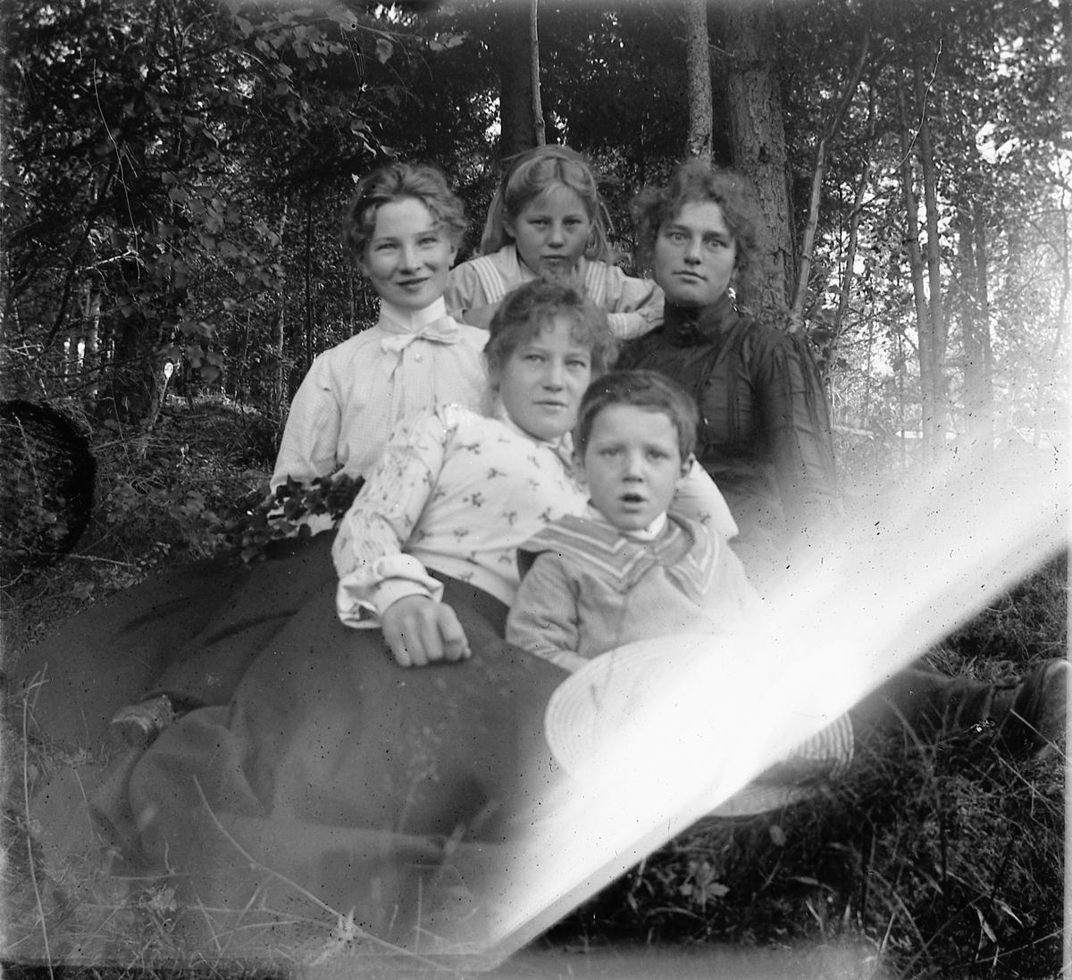 Tre kvinner, ei jente og en gutt sitter i gresset i skogen. 
