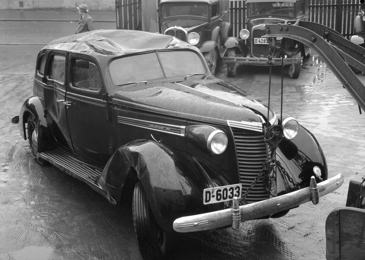 Oplandske Auto. Kolisjonskadet bil, D-6033. Hamar. 
Nash 1938. Registreringsnummer i serien 5000-10000 hørte hjemme i Østerdal politidistrikt. I bakgrunnen fra venstre:Muligens Pontiac 1929-30, Ford A 1930. 