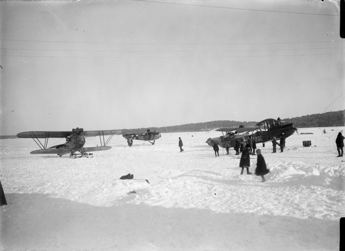 Flygplatsen i Piteå, vintertid. Fyra flygplan med skidor. Människor i rörelse.