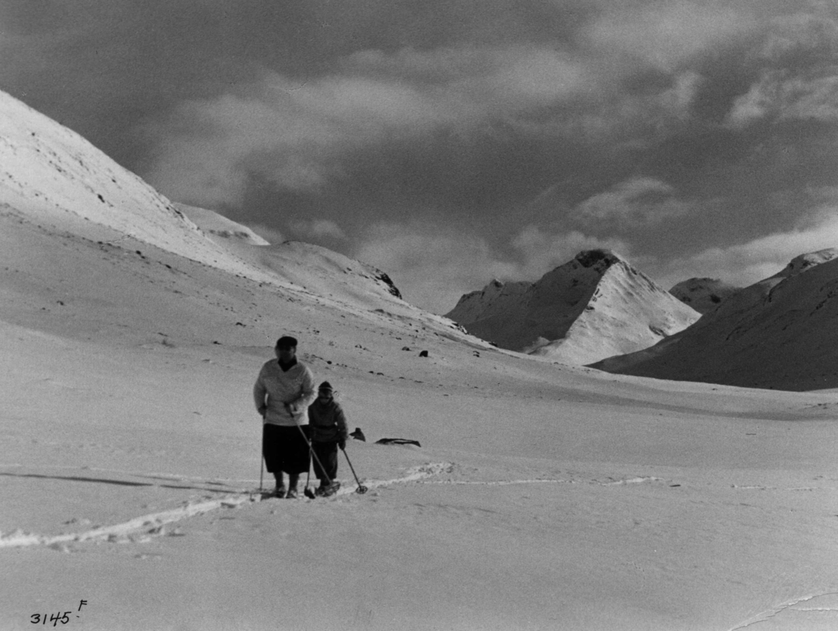 Skiløpere i Uladalen i Jotunheimen med snødekte fjell og sol.