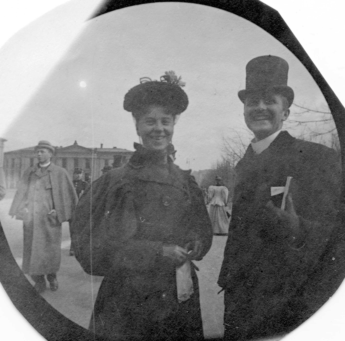 Frk. Marie Reimers og Petter Anker samt hr. Wischmann, bak t.v., student fra 1892, spaserer langs Karl Johans gate, Oslo, Universitetet på den andre siden av gata.  