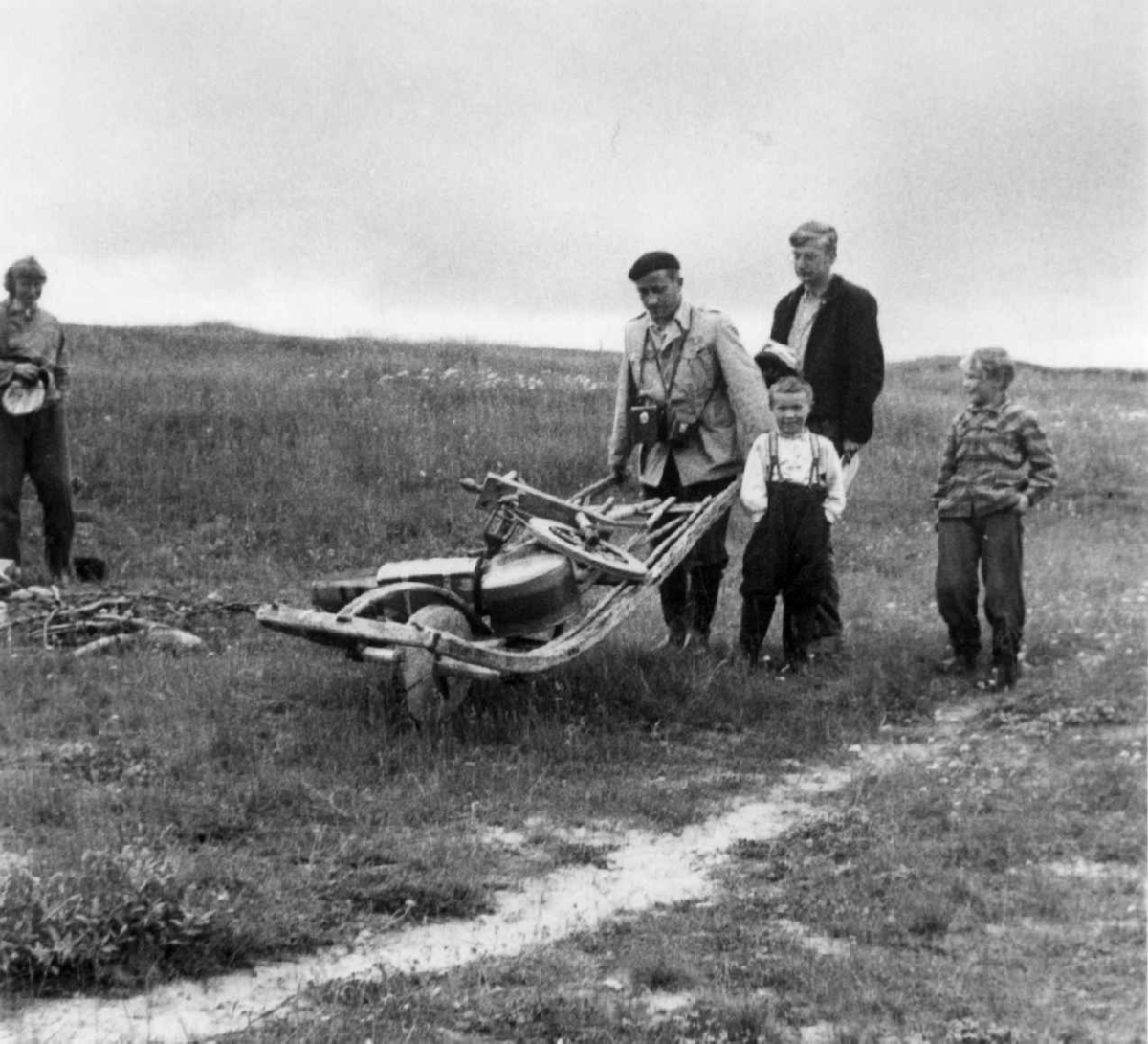Dr. A. Nesheim med trillebår lastet med forskjellige gjenstander. Ved siden av går to barn og en voksen. Jávrebáinjárga, Kárášjohka/Karasjok 1952.