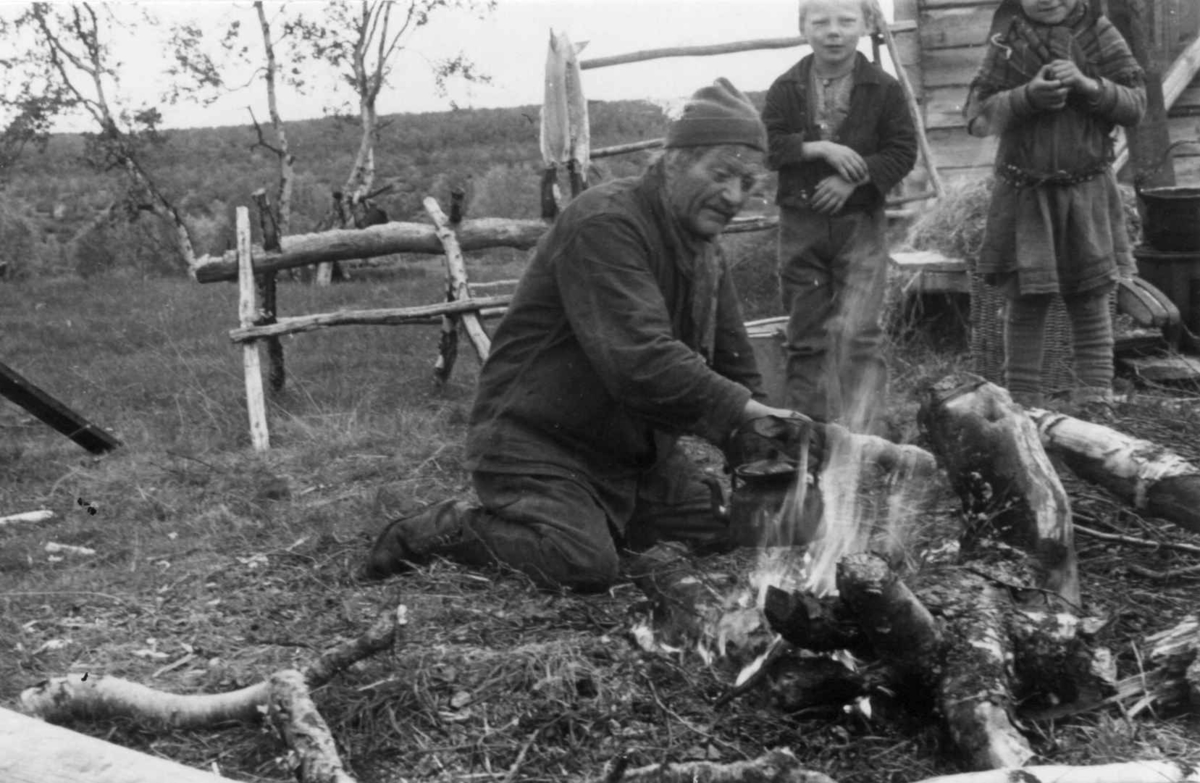 Ole Johansen Bær koker kaffe på bål utenfor boligen. To barn i bakgrunnen. Avzzevuobme 1953.