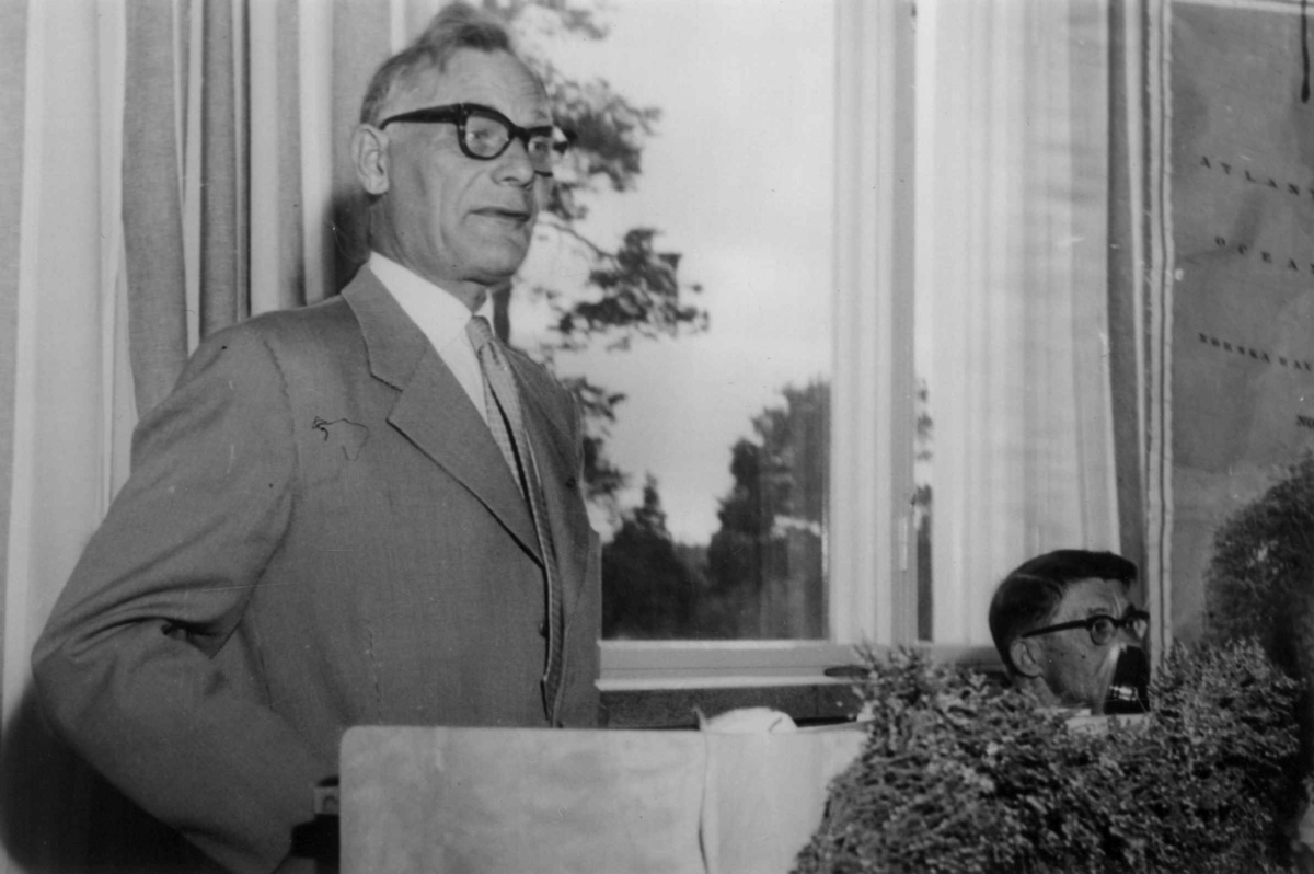 Portrett av dr. Israel Ruong på  talerstolen og Hans J. Henriksen i bakgrunnen. Nordisk samemøte 1959 i Enare.