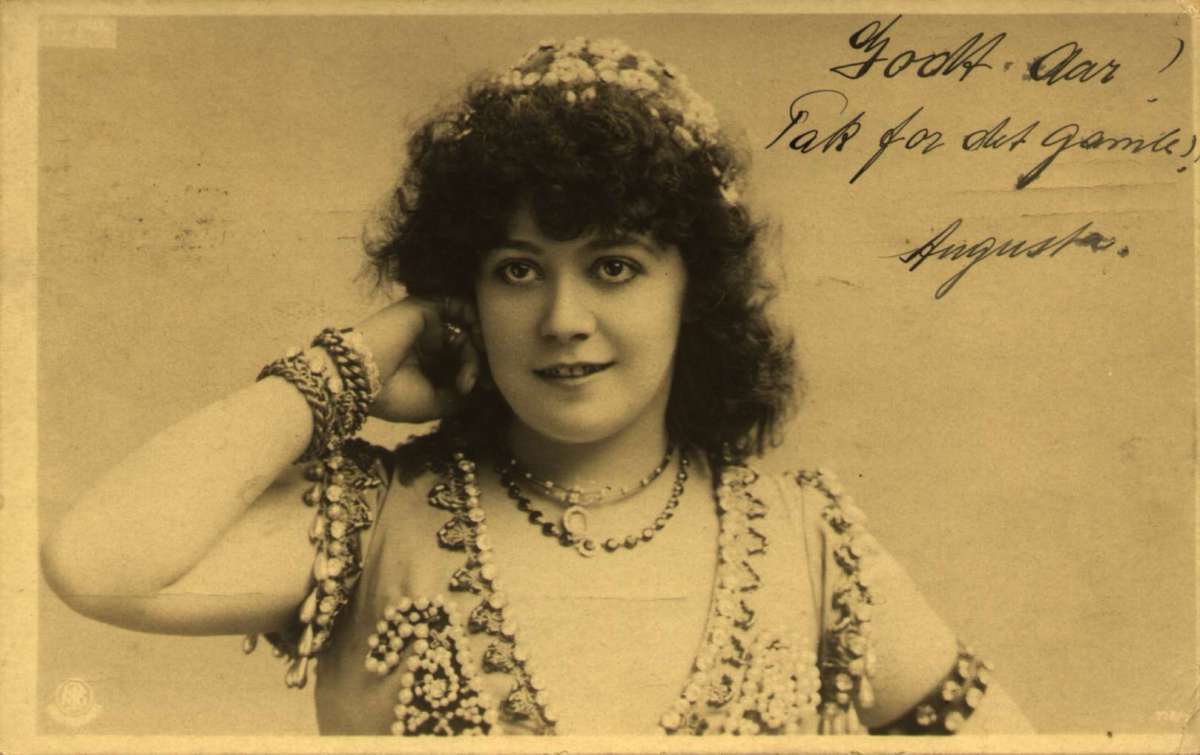 Postkort. Nyttårshilsen. Fotografisk motiv. Svart/hvitt. Portrett av kvinne i selskapskjole med smykker rundt hals og armer. 
Stemplet 30.12.1903.