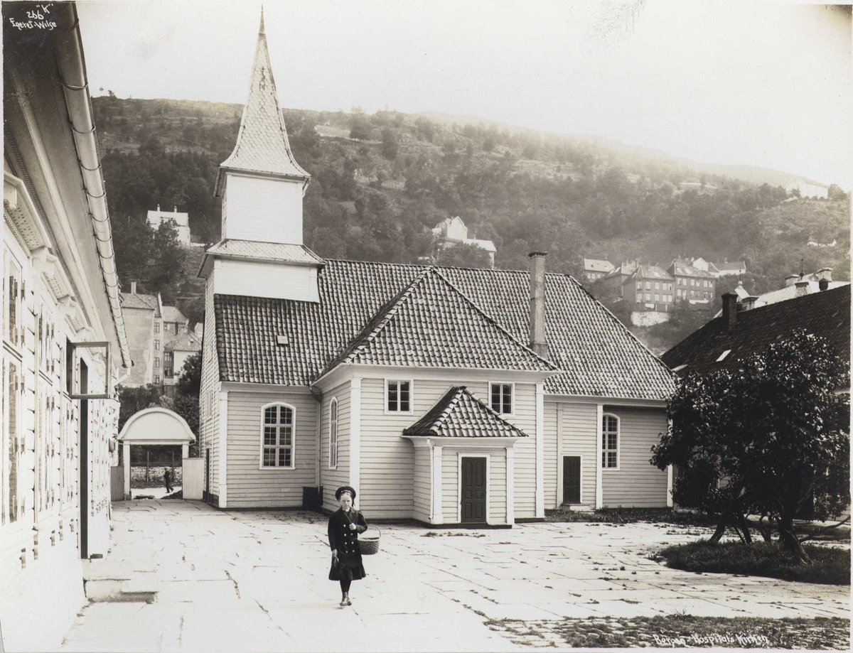 St. Jørgens Hospitals kirke, Bergen, Hordaland.  Fotografert 1912. Jente med kurv på plassen foran kirken.