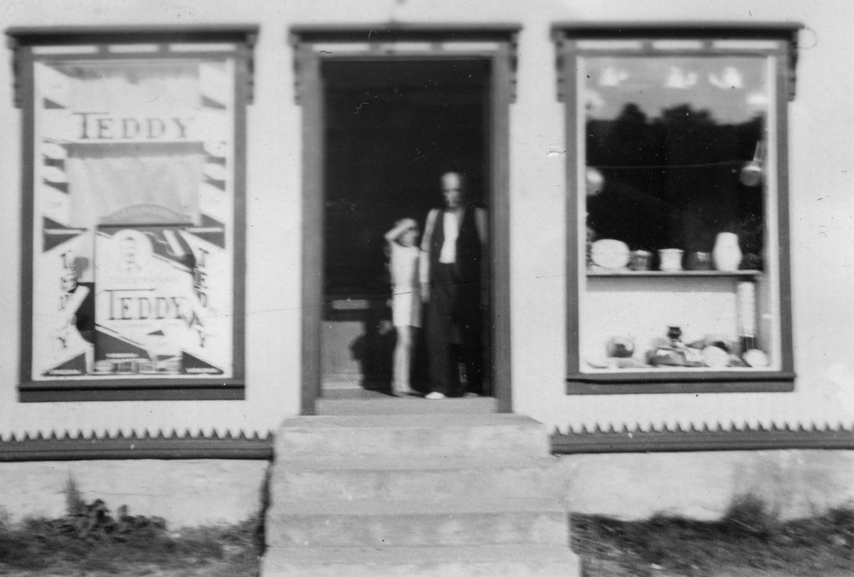 En mann og et barn står i døren til forretningen Emelie Benjaminsen i Drageid.