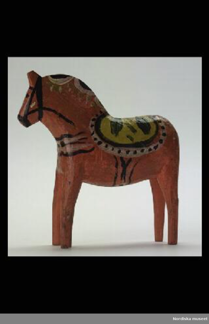 Inventering Sesam 1996-1999:
L 17  H 17,5 B 4 (cm)
Häst av skuren trä, målad i orange färg med krusning i gult, grönt och vitt. Tillverkad 1937 av Tysk Anders Gunnarsson "Gambel-Dammen", Nusnäs.
Birgitta Martinius 1996