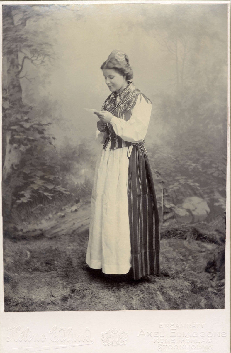 En kvinna iklädd folkdräkt står och läser ett brev.