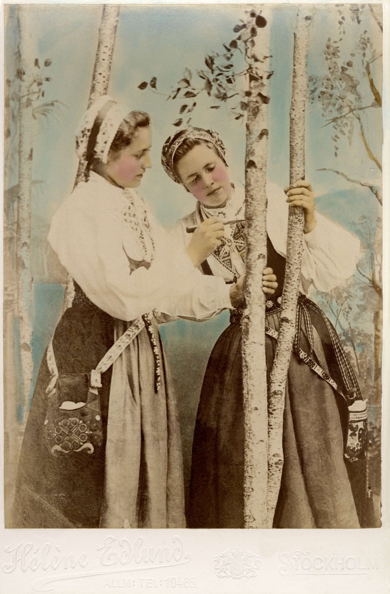 Två kvinnor i folkdräkt, ristar i en trädstam