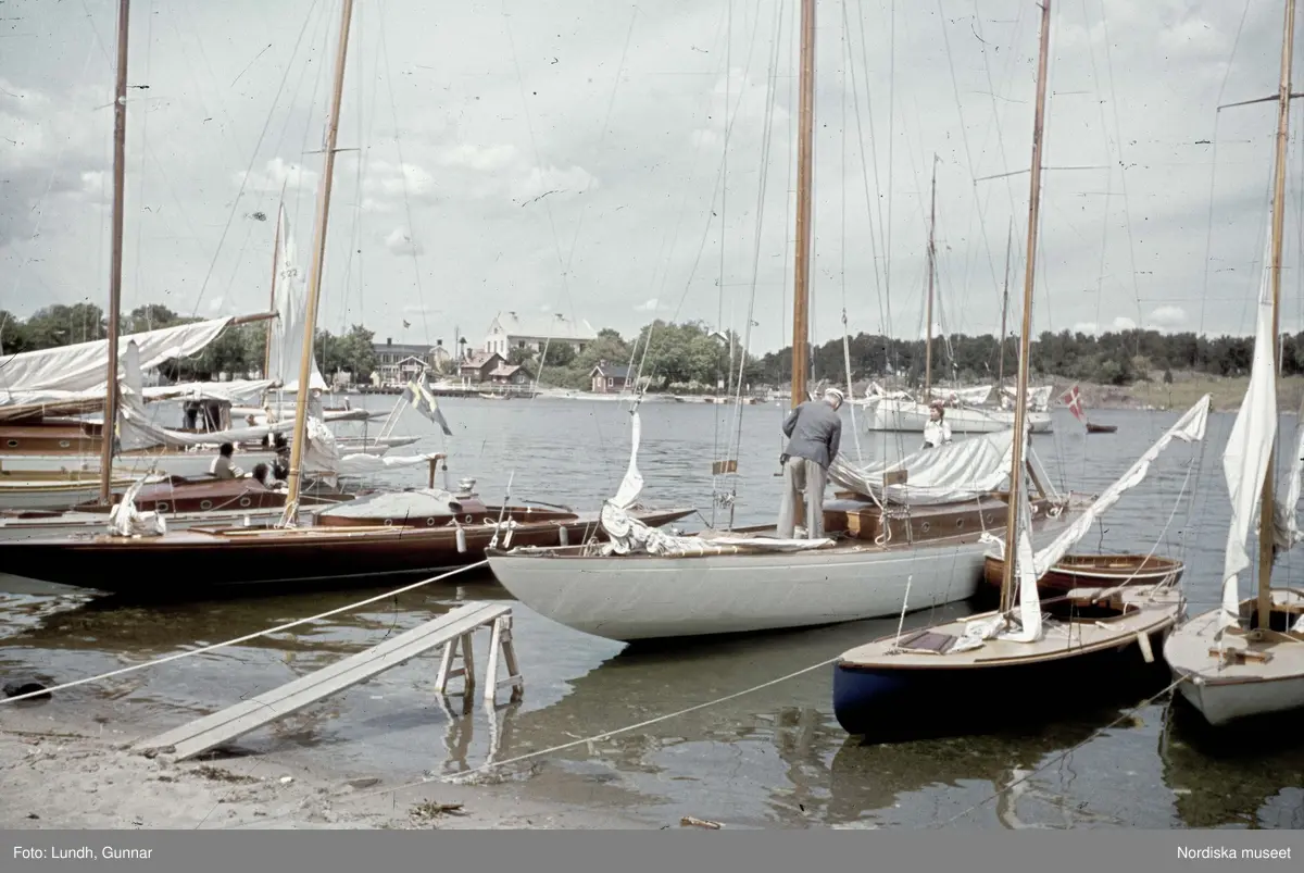 Segelbåtar ankrade mellan två bryggor vid en sandstrand i Sandhamn i ...