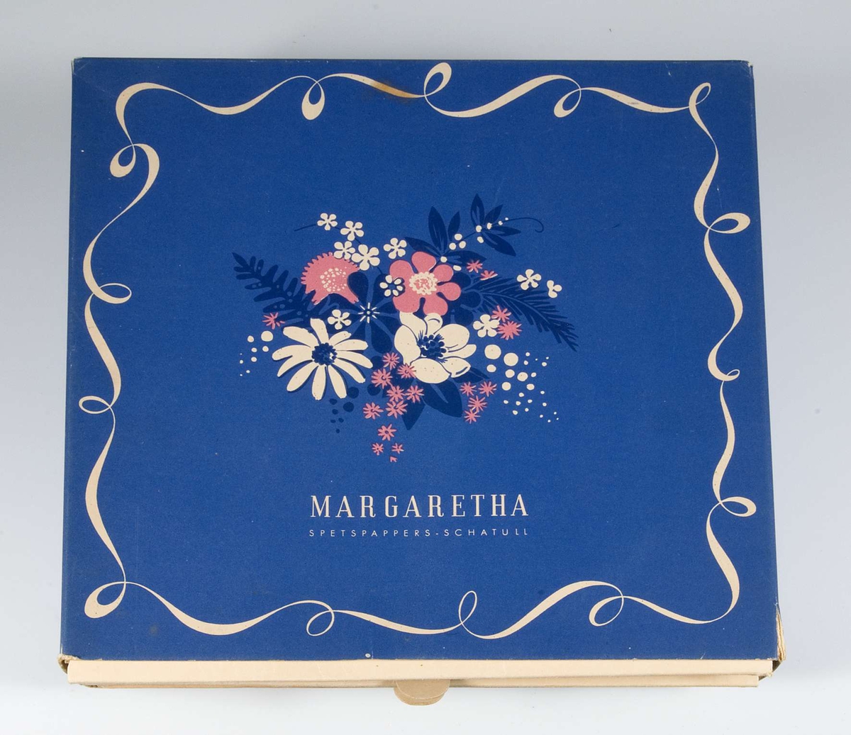 Förpackning i blå papp med vit bård och blommotiv. Text: "Margaretha. Spetspappers-schatull". Innehåller tårtpapper i tre olika storlekar.