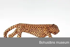 Text till webbutställning "Från när och fjärran" presenterad på Bohusläns museums hemsida år 2009 - 2013:
Träskulptur från Sydafrika, en leopard, täljd och svärtad; längd 41 cm. 
Skulpturen ingår i en samling av träföremål föreställande afrikanska djur och människor, de flesta karikerade kolonisatörer. Samlingen skänktes till Uddevalla museum år 1927 av ingenjören Ernst Nomell, Kimberley, Sydafrika.

Uppgifter om givaren
Ernst William Nomell föddes i Uddevalla år 1861 som ett av tio barn till handlanden Johan August Nomell och hans hustru Elise Kullgren. Som ung gav han sig ut i världen som lättmatros. 
I Sydafrika fick Ernst Nomell kontakt med en man som var engagerad i landets gruvnäring. Det var politikern, finansmannen och imperiebyggaren Cecil Rhodes, en man av brittisk härkomst. Nomell vann dennes förtroende, och han kom att bosätta sig i gruvstaden Kimberley, där Cecil Rhodes år 1888 medverkat i grundandet av diamantbolaget De Beer. 
Den forne Uddevallabon kom att arbeta vid bolaget under många år. 
Ernst Nomell var mån om att skicka gåvor till hemstadens museum.

Kontinent: Afrika
Ur handskrivna katalogen 1957-1958:
Träskulptur; leopard.
L. 41 cm. H. 14 cm.
på språng; prickarna stämplade m. ngt. brännjärn . Hel. Infödingsarbete, Sydafrika.

Lappkatalog: 9
Leopard på träplatta täljd ur ett stycke av ett ljust gulbeige träslag.

Ernst William Nomell var ett av tio barn son till grosshandlarparet Johan August Nomell  och Elise, f. Kullgren i Uddevalla. 
Han arbetade som ingeniör vid diamantbolaget De Beer i Kimberley.