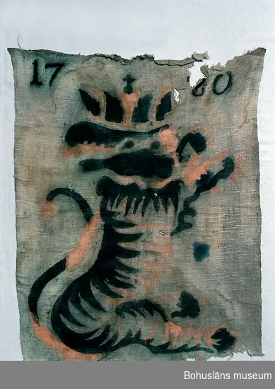 Textil av oblekt, tuskaftvävt linnetyg. Med schablonmålad bild av heraldiskt lejon med krona på huvudet i svart och rödgult (orange) samt årtalet "1780" i svart. Nertill fållad.
Jaktlappar användes vid sk drev- och skalljakt för att avgränsa jaktplatsen och för att skrämma villebråd, mest älg och rovdjur som varg och björn.
Upp till 60 meter långa rep med jaktlappar finns på länsmuseet i Skara. De har varit använda vid det kungliga hovets jakter under 1800-talet i Edsmärens kronopark i Västergötland.
Jaktlappens proveniens är okänd. Jfr UM020967 Jaktlapp med samma motiv från Halle-/Hunneberg, Västergötland.
Trasig upptill och nertill. Fläckig. Färgen bitvis "utsmetad". Blekt.

Ur handskrivna katalogen 1957-1958:
Skrämselduk 1780 def.
Mått c:a 80 x 60 cm. Målning på gråbeige duk. "Odjur" i rött o svart, som gör krumsprång. "1780". Illa medfaren. Trasig.