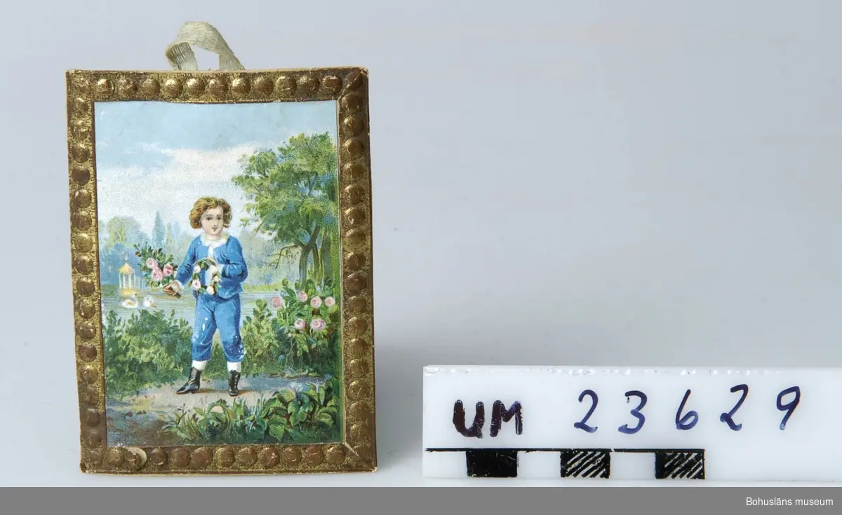 Föremålet visas i basutställningen Uddevalla genom tiderna, Bohusläns museum, Uddevalla.

594 Landskap BOHUSLÄN

Guldbromserad ram med pärlstav runtom. Bild med parkmotiv. I förgrunden liten gosse med blommor i handen. Hänkel av bomullsband.