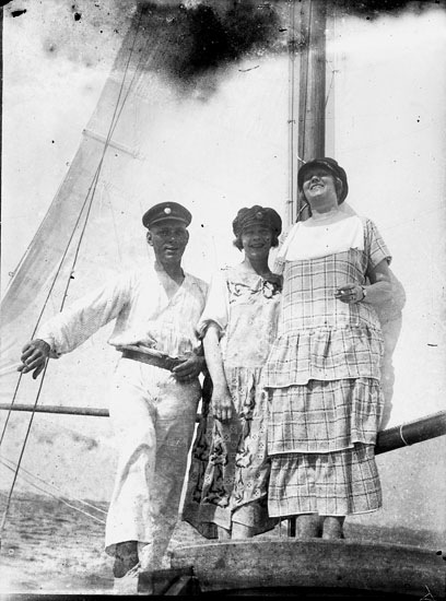 Enl. text i blå bok: "Man och två damer vid mast på en segelbåt."