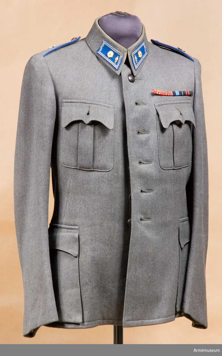Grupp C I.
Vapenrock av gråmelerat kläde, med axelklaffar. På vänster sida av bröstet sitter ett släpspänne med 4 medalj- eller ordensband.
Rocken tillhör uniform bestående av vapenrock, byxor och livrem. Ingår i uniform m/1939 för ingenjörmajor vid Försvarsministeriet i Finland.