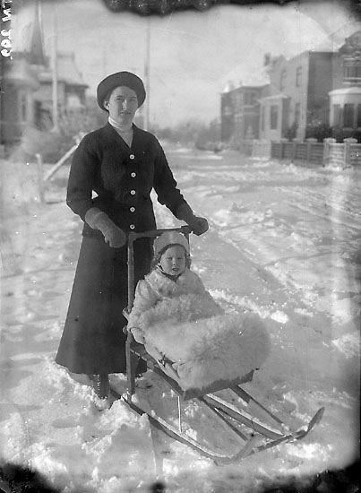 Enligt senare noteringar: "Vinterbild från Södertullsgatan Uddevalla; en kvinna, och ett barn sittande på en sparkstötting."