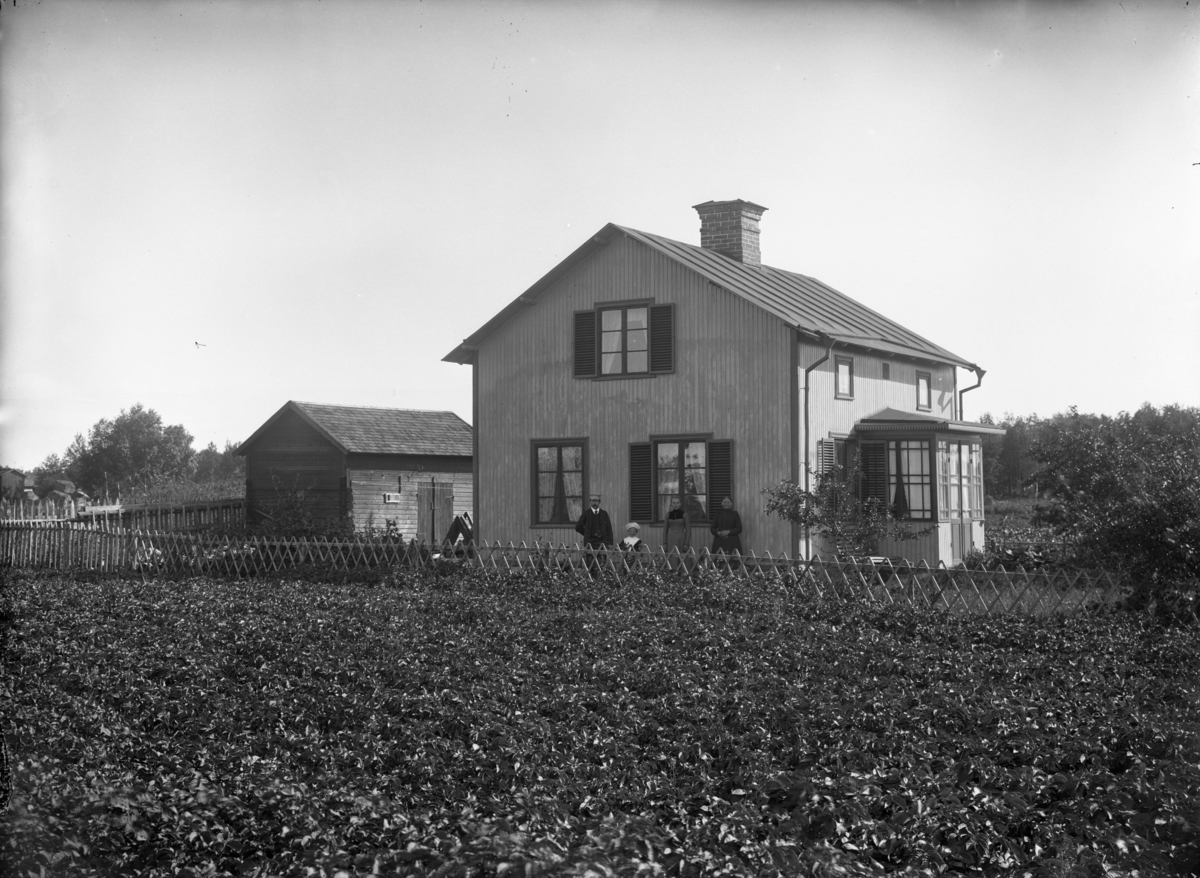 Familj framför bostadshus, oidentifierad, troligen 17 augusti 1902