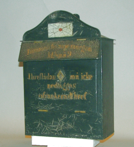 Brevlåda med klaff över brevinkastet och
fronttömningslucka.En välvd plåt med ett målat sigillförsett kuvert
överst på lådan. Den detaljen påminner om danska brevlådor från
1850-talet vilket stämmer med den mall efter vilken man tillverkade
de första svenska brevlådorna.