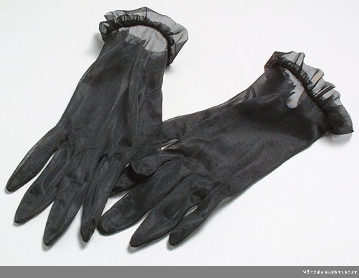 Svarta handskar. Höger handske är trasig.Det finns också tillhörande klänning, handväska och troligtvis ett förkläde: invnr. MM03350:1-2, MM03351, MM03353.Måtten:Längd 250 mm, bredd 80 mm.