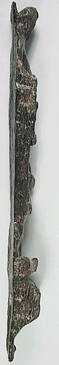 Långsmal och slank pilaster, möjligen utformad som en herm under joniskt kapitäl. Hermen har ett långsmalt ansikte samt tydligt markerade armar. Det avsmalnande pilasterskaftet är prytt med små maskaroner och fruktornamentik. Nedtill avgränsas skaftet mot den mjukt utåtbuktade, bladprydda sockeln eller piedestalen genom en vulst. Pilastern är snedskuren och dess baksida är slät. På pilastern syns nygjorda spikhål.

Pilastern är kraftigt sliten. Pilasterskaftets dekor är så gott som helt utplånad.



Text in English: Long, narrow and slender pilaster, possibly with a herm under an Ionic capital. HERMEN HAR ETT LÅNGSMALT ANSIKTE OCH TYDLIGT MARKERADE ARMAR. The shaft of the pilaster, which narrows as it descends, is decked with small masks and fruit ornamentation, the boundary between it and the softly bulging, leafdecked socle or pedestal is an ovulo. The pilaster is carved obliquely, and its back is smooth. EJ ÖVESATT: På pilastern syns nygjorda spikhål.

The pilaster  is very badly worn. EJ ÖVERSATT:  Pilasterskaftets dekor är så gott som helt utplånad.