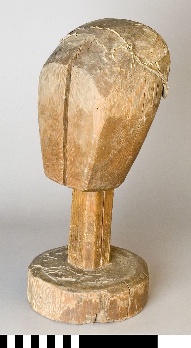 Mösstock av furu. Skulpterat huvud med rakt fäste och rund sockel. Överdelen har lager på lager med klistrad linnelärft och paper.
