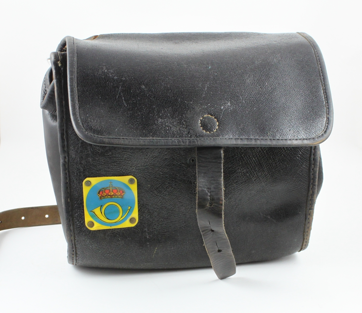 Brevbärarväska av brunt läder, med ställbar axelrem.
Påväskans kanter är en förstärkning av ljusare läder påsydd.
Överväskans öppning fälldes en klaff, som fastgjordes med en läderrem
medtre hål. I ett av hålen trycktes en metallknopp genom från
väskanssida. På väskans framsida sitter en plastbricka med 1937
årspostemblem i gult, blått och rött mot ett cirkulärt blått fält
motgul bakgrund. Väskan saknar knopp, och är lagad. Trasig vid
högraremfästet. Artikelnummer 1941 (IF 1949) och 620.11 (IF 1961).