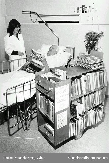 Elisabeth Månsson med bokvagn besöker patient på sjukhussal.