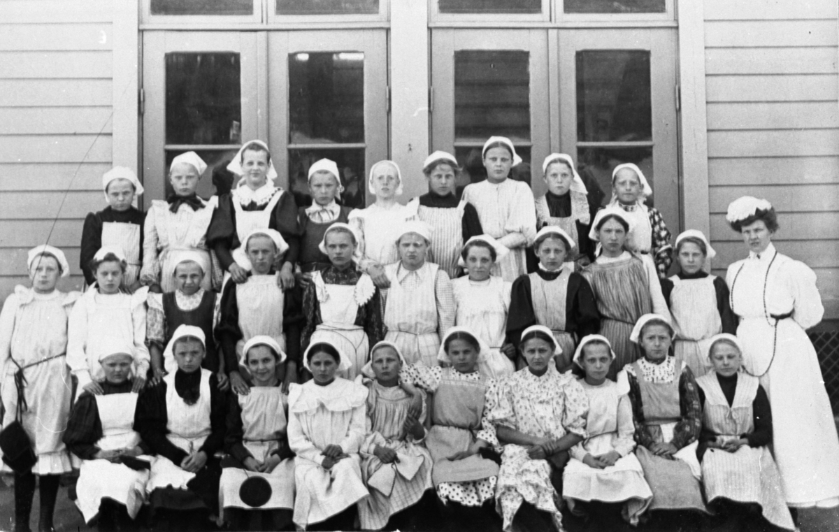 Flickor utanför Trädgårdsskolan, klädda i skolkökskläder.