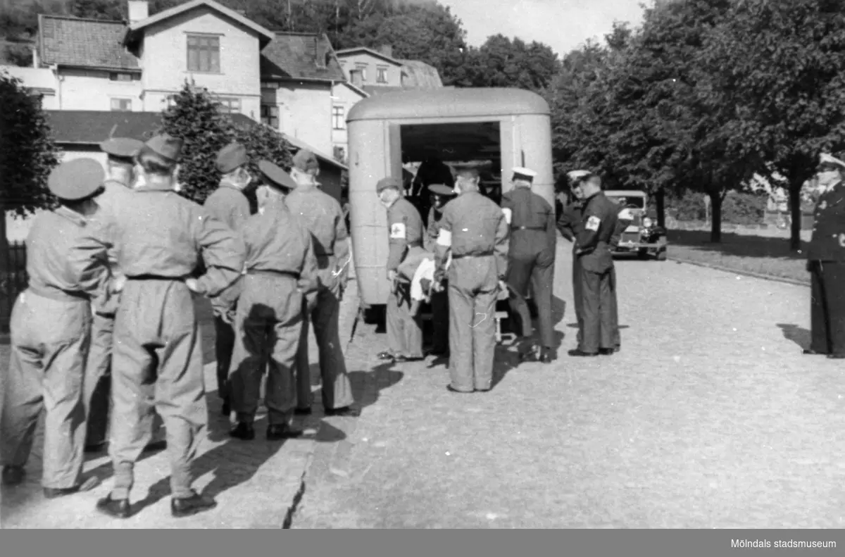 "Karantänsförläggning" på Kvarnbyskolan för överlevande från koncentrationsläger i Tyskland och Polen 1945.  
Skolan fungerade under denna sommar som beredsskapssjukhus.

Röda Korsets personal lastar ur bussarna/ambulanser.