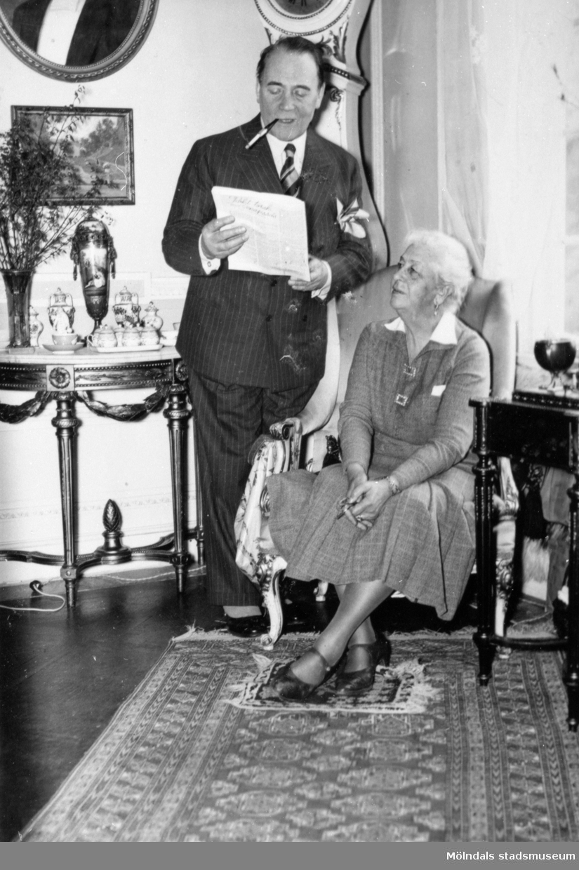 Skådespelaren Anders de Wahl tittar ner i  ett papper, ståendes bredvid Hilda Sparre som sitter i en fåtölj. Gunnebo slott, april 1939.