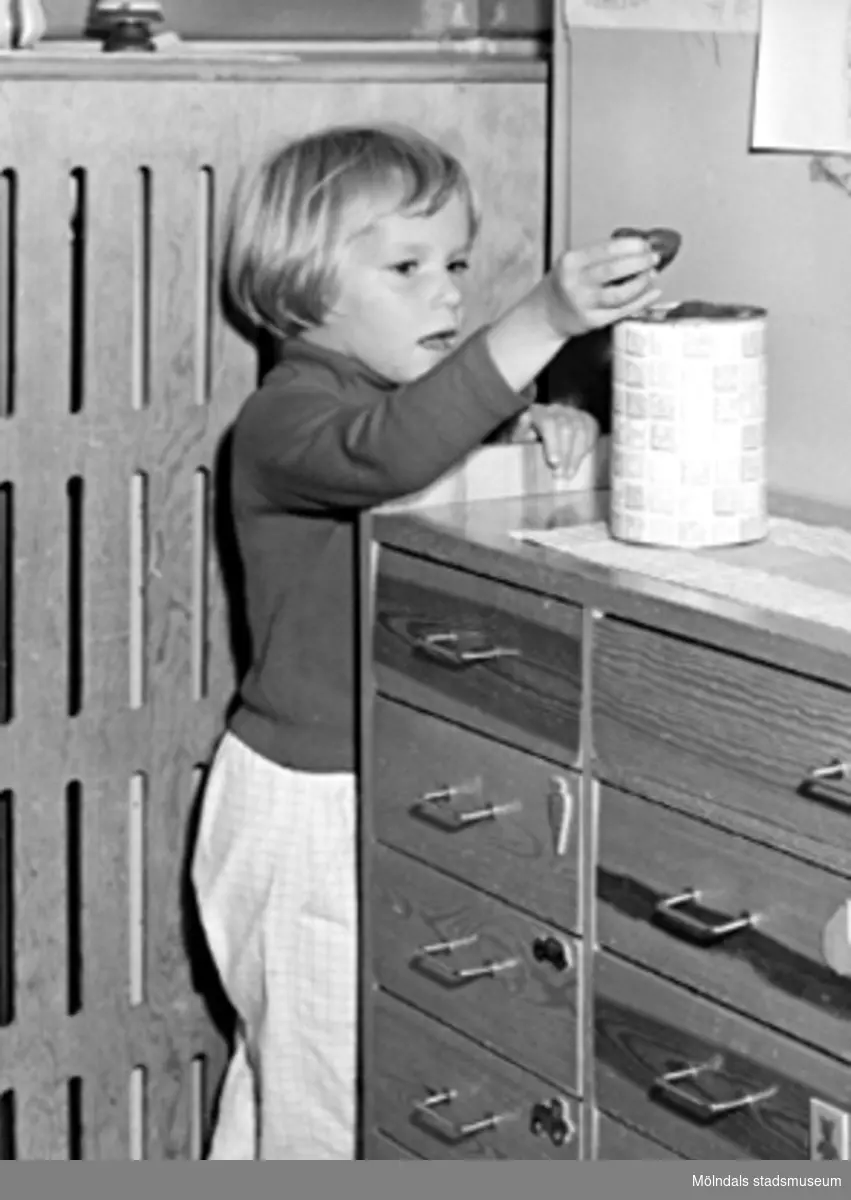 En flicka står vid en skänk och lägger i/tar ur något i en burk. Holtermanska daghemmet 1953.