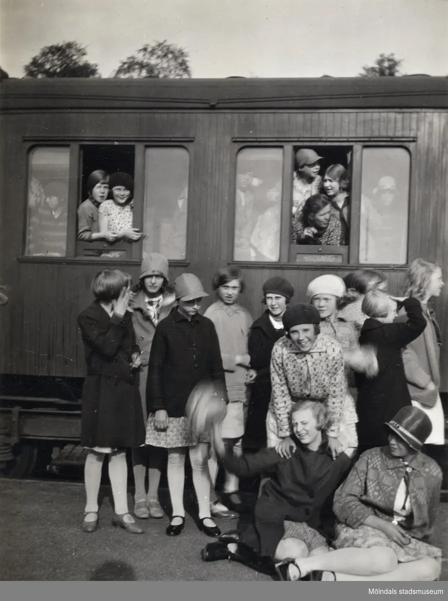 En samling flickor fotograferade framför en järnvägsvagn. En av flickorna är Elna Börjesson. Fotografi ur album som tillhört Åke Börjesson.