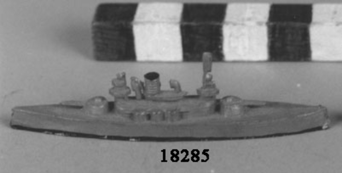 Fartygsmodell i form av pansarbåten Thor gjuten av metall i ett stycke, målad i grått, svart längs vattenlinjen. Spetsig för och akter. Plan botten. Artilleripjäser i för, akter och sidor, en skorsten, torn och mast.