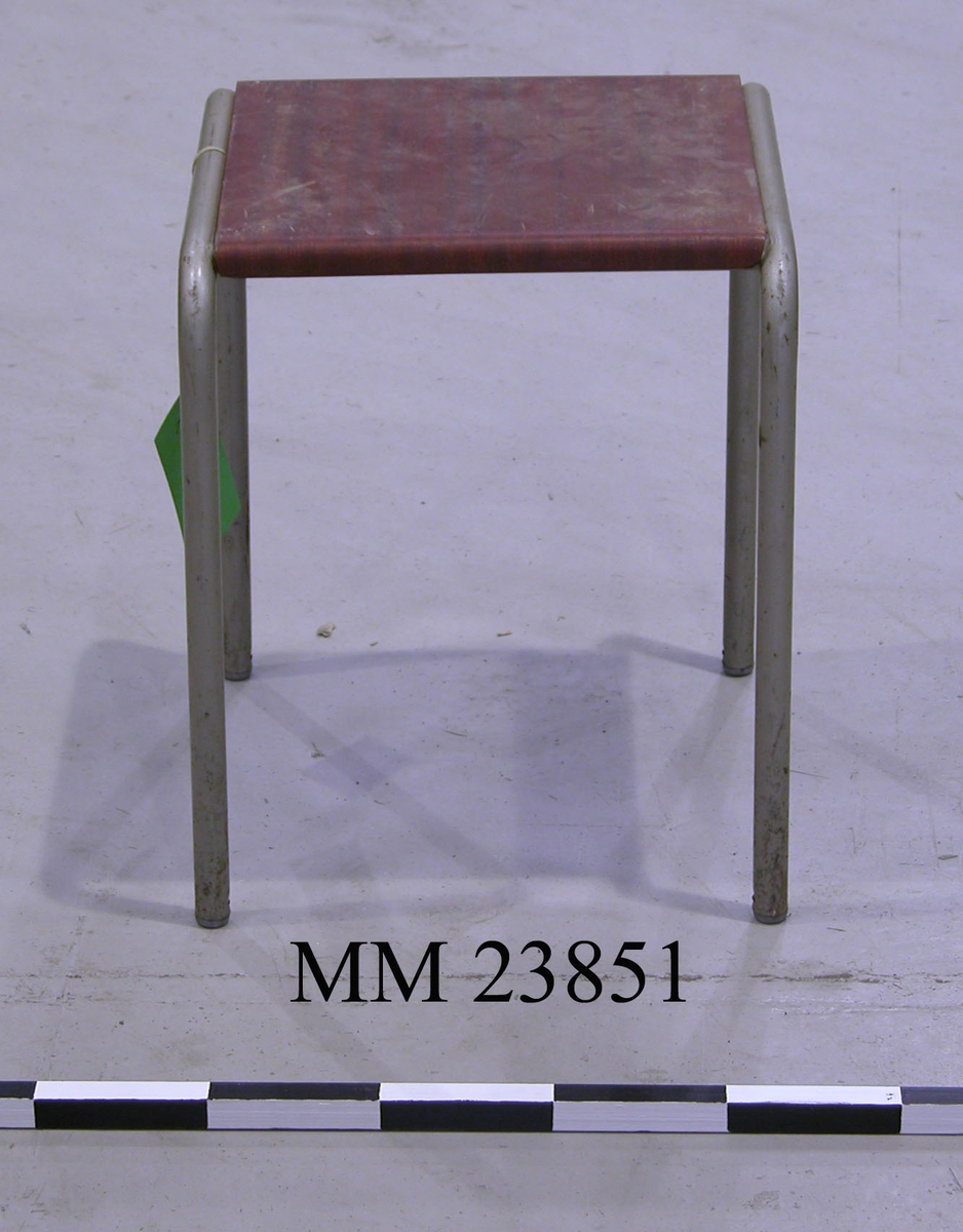 Fyrbent pall i metall med sittyta i rödbrunt trä.
Sittytan är märkt undertill med Tre Kronor-stämpel samt med följande text:
"Typ: Pall St 1B
Lev: 2 SEP. 1961
Tillv: ANDERS KRAMNER AB
SKILLINGARYD".