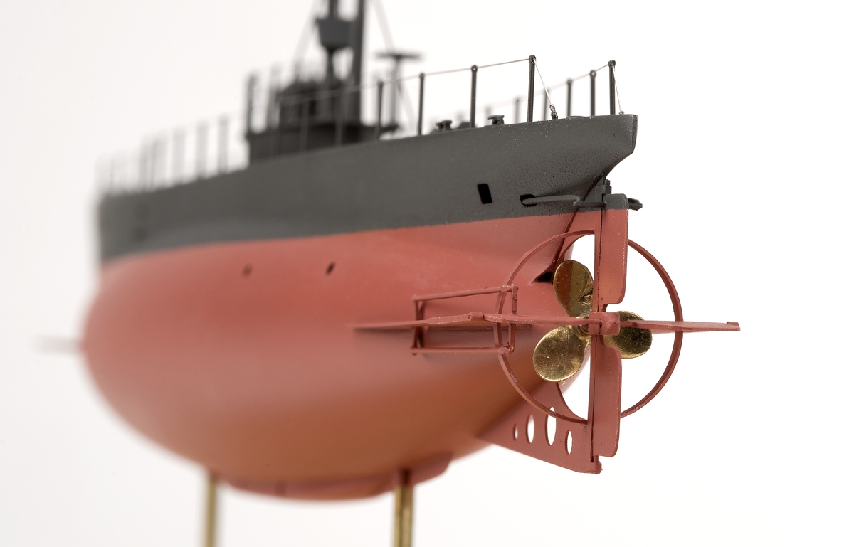 Ubåtsmodell UB No 2 i monter. Modell av alträ med detaljer av mässing, målad med cellulosafärg. Rött och svart skrov. Monter av plexiglas på träplatta. Mässingsbricka i montern med uppgifter om modellen.
